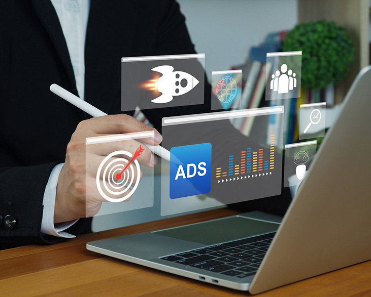 Person using a stylus with a laptop, interacting with floating digital icons representing online advertising, analytics, targeting, and audience insights.