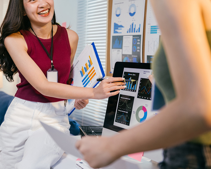 woman presenting marketing data on a computer screen while smiling and discussing charts with a colleague